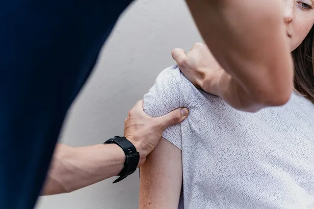 A therapist supporting a patient's shoulder during a movement assessment