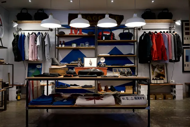 A small shop interior with a single rail of clothing, open shelving and pendant lights