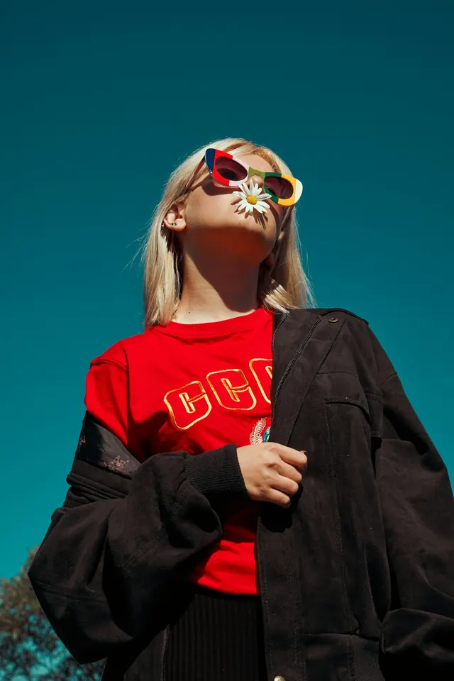 A person in a vivid red knit under a dark jacket, looking up against a deep teal sky