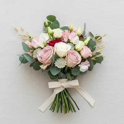 A blush and cream hand-tied bouquet of pale roses, lisianthus and sweet pea with eucalyptus, laid flat on ivory linen