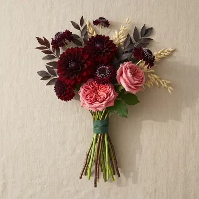 A deep red and burgundy hand-tied bouquet of dark dahlias, garnet roses and plum scabiosa laid flat on ivory linen